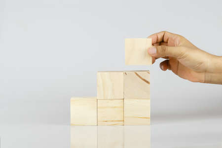 hand holding wooden block arranging step white background, stacking wood grow success.