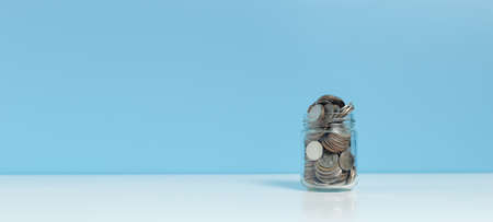 Coins in glass bottle put on table blue background, growth save or investment concept.の写真素材