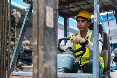 Man wear safety helmet happy smiling looking at camera driver forklift warehouse in factory. Male worker industrial operate. control loading container box. logistics export import concept.の写真素材