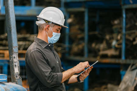 Engineering man wear face mask using tablet at factory. Heavy industry worker man concept. warehouse...