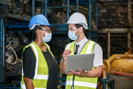 Team engineering two nationality wear face mask uniform working with computer laptop at factory....
