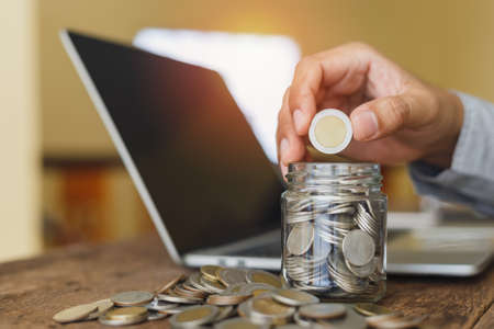 Coins in glass bottle put on table with hand putting money coins at office table, growth save or...