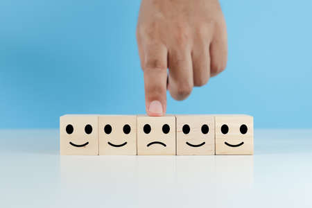 hands of man finger pointing selection wooden cube blocks with unhappy emotion icons blue background. personnel not selected of corporate. rating and ranking business concept.の写真素材