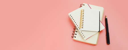 stack of empty notebook and pen for to do list on pink background, workspace for text top view. banner copy space.の写真素材