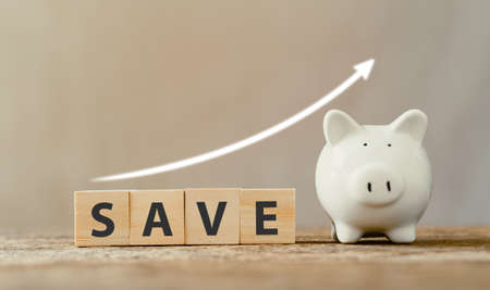 Wooden cube word "save" with arrow pointing up and white piggy bank. savings money and grow up for future concepts.の写真素材