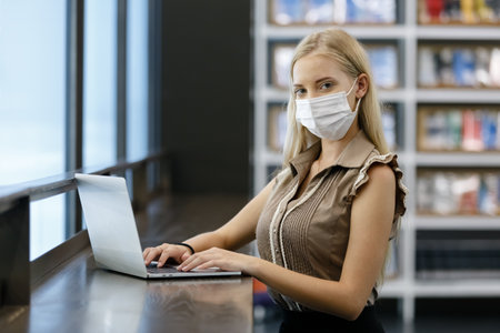 Beautiful woman with blond hair wear medical mask using with computer laptop at office table. professional freelancer in workplace.の写真素材