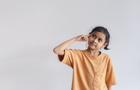 asian child girl wear orange T-shirt pointing to head gesture thinking. Thing ideas concept. Copy space use for text media advertise.の写真素材