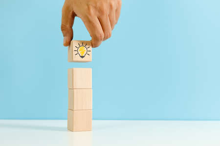 Hand holding wooden cube block with Light bulb icon blue background. symbol of creativity, Ideas and...