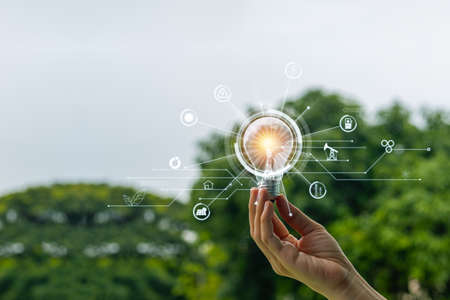 Hand holding light bulb nature background with energy power icons. Energy power electric environment from nature concept.の写真素材