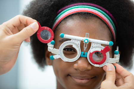 close up opthalmology trial frame with young woman african american eye test ophthalmological in optics clinic. woman checkup eye health with equipment opthalmology medical in hospital.の写真素材