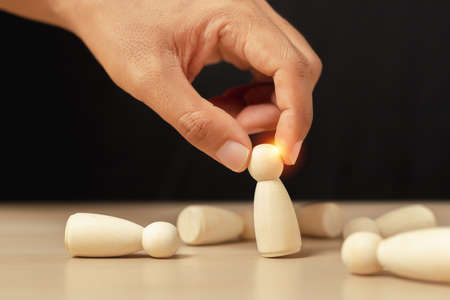Wooden figures human was chosen leadership of teamwork. man's hands are select wooden puppet to...