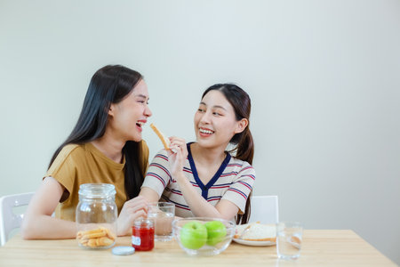 happy asian female couple have breakfast at table kitchen. two beautiful woman eating food in the morning.の写真素材