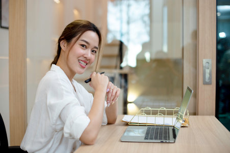Happy smiling young asian businesswoman sitting at office table. Female smile looking at camera. success smart woman working in corporate.の写真素材
