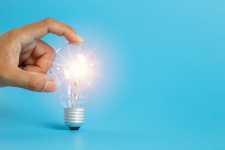 Economical energy concept. Hand holding light bulb on blue background. electricity power innovation....