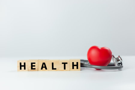 Diagnosis cardiologist concept. Text health on wooden cube blocks with red heart and stethoscope on white background. Equipment check heartbeat and pulse of patient.の写真素材