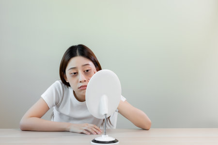 Asian young female stress looking mirror have dark eye circles from staying up sleepy late. from hard work, no time to sleep.の写真素材