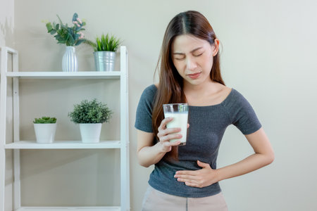 Asian female holding glass milk and hand touching abdominal area stomach ache after drinking milk. symptom lactose allergy and calcium. cow's milk allergy.の写真素材