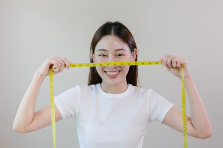 Asian woman holding a tape measure yellow around her waist. female happy smiling with tape measure put on face look at camera.の写真素材