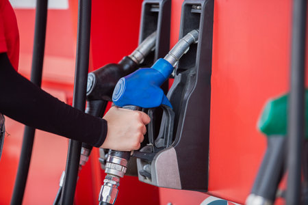 close up hand of woman holding pump nozzle for service at gas station. male employee worker fueling oil car. business energy concept.の写真素材