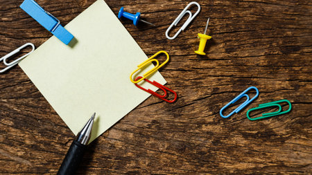 Empty sticky post note paper with pen pin and paper clip sheet on wooden office table.