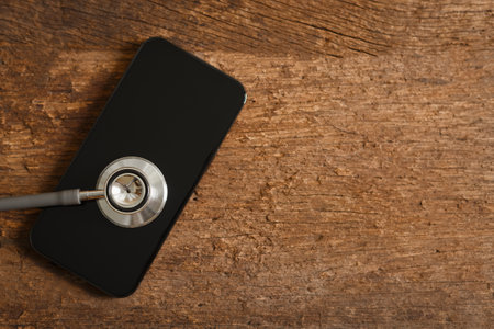 stethoscope over smartphone on wooden background. clinic check treatment online, health and care...