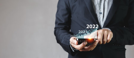 Businessman touching smartphone screen with growth graph year 2022. stock exchange analyzing chart. information statistics diagram profit global financial marketing. investment and marketing concept.の写真素材