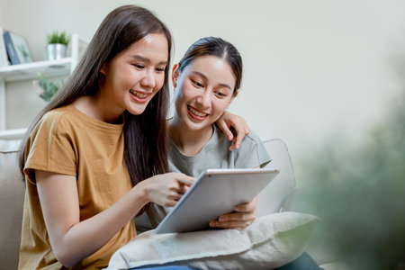 happy female couple using digital tablet shopping online sitting on sofa at home. beautiful woman girlfriend lifestyle. two girl looking movie online.の写真素材