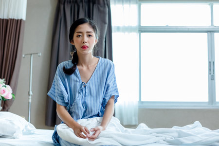 asian young patient women gloomy mood sitting on bed at hospital private room. unhappy from illness. medical health care insuran.の写真素材