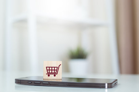 Online shopping concept. wood cube block with shopping cart icons over on mobile phone, use smartphone connection marketplace consumer service.の写真素材