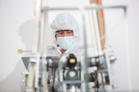 Machine staff, mask production department. Engineer wearing protective suit Inspecting quality of...