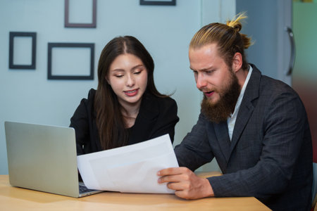 Male manager using laptop to give work instructions to female secretary at office. Discussions,...
