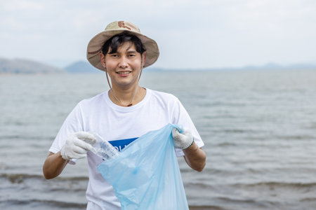 Male volunteers collecting garbage looking at camera, conducting environmental cooperation, saving world reducing global warming, Volunteers clean plastic bag waste in natural attractions.の写真素材