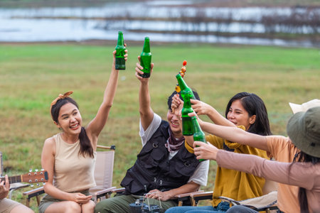 Group of young Asian friends party on vacation enjoy cheering with beer bottle. drinking at camping lake side. hands holding alcoholic beverages. Picnic in holiday.の写真素材