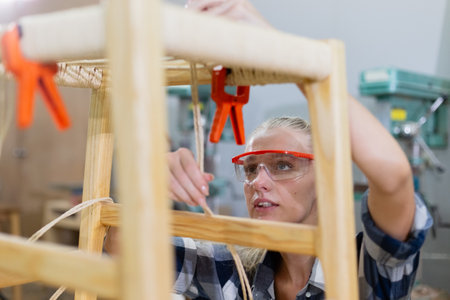 Female worker working furniture at manufacturing wooden industry. Women carpenter wear uniform and goggles profession in wood factory.の写真素材
