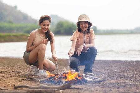 Two Asian girls making bonfire enjoy camping near lake relax vacation. Female enjoy fun in holiday.の写真素材