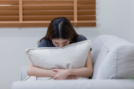 Female having depression sitting alone in bedroom corner. woman headache unhappy emotion. Sitting alone on sofa. woman with depressed embracing pillow. Anxiety despairing mental health problems.の写真素材