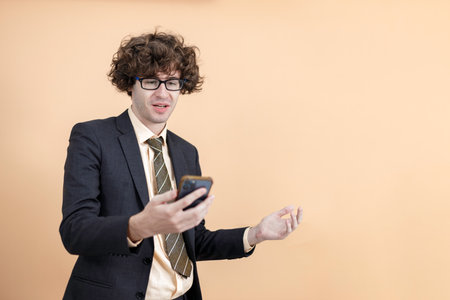 Cheerful young businessman wear spectacles in suit posing surprised and wonder looking at smartphone...