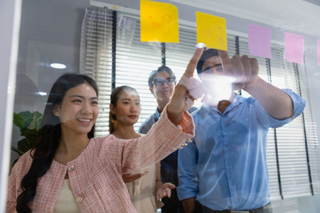 Business team meeting planning new strategy using colored sticky notes on mirror board in workplace,...