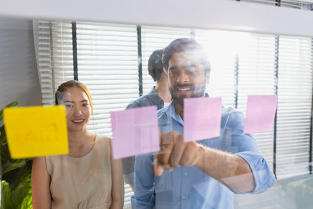 Business team meeting planning new strategy using colored sticky notes on mirror board in workplace,...