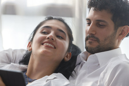 happy couple middle aged man and woman hugging lying digital tablet relaxing on sofa in modern house living room. browsing internet watching movie and serie in holiday.の写真素材