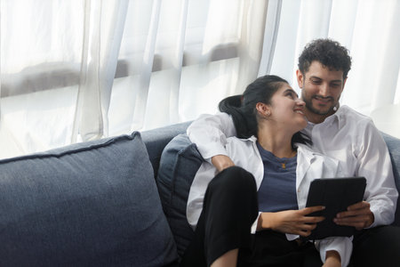 happy couple middle aged man and woman hugging lying digital tablet relaxing on sofa in modern house living room. browsing internet watching movie and serie in holiday.の写真素材