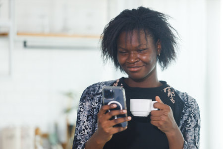 Portrait of attractive woman african american businesswoman holding coffee cup using mobile phone standing office. searching reading  information. Working chatting online with smartphone.の写真素材