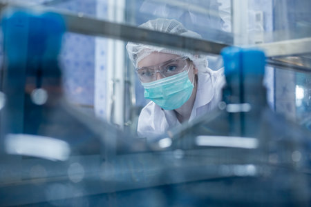 Female worker using tablet checking quality drinking water before process of filling water into plastic bottles to bring out to consumers. Water bottles on production line of factory.の写真素材