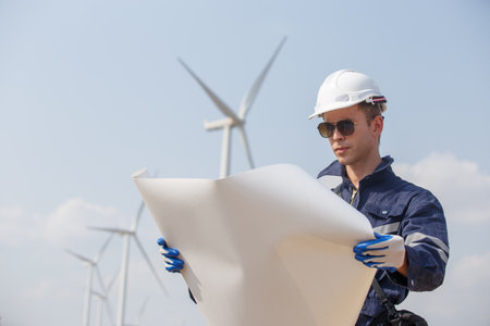 man engineer worker wearing safety uniform holding and reading blueprint working about renewable energy at station energy power wind. technology protect environment reduce global warming problems.の写真素材