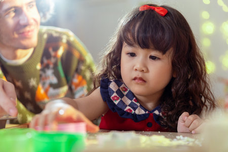 Happy family christmas day. Parents and daughter celebrate Christmas happily in their own home. Little girl enjoying make cookie bakery desserts on food table holiday merry festive activities.の写真素材