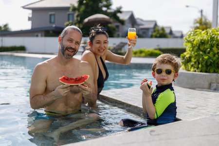 Happy vacation kid boy eat watermelon with family parent have fun enjoy at swimming pool. father and mother with son cheerful activity relaxing in summer holiday.の写真素材