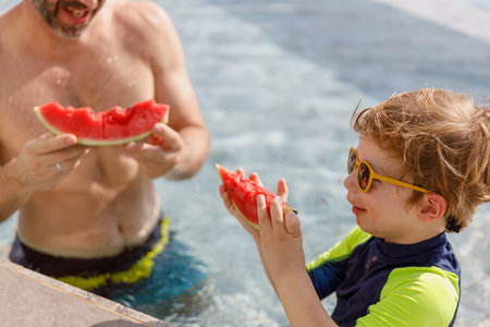 Happy vacation kid boy and father eat watermelon have fun enjoy at swimming pool. children and parent cheerful activity relaxing in summer holiday.の写真素材