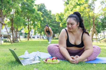 Asian female in sportswear training exercise on mat looking preview with laptop. woman training online practice yoga in park. concept of healthy.の写真素材