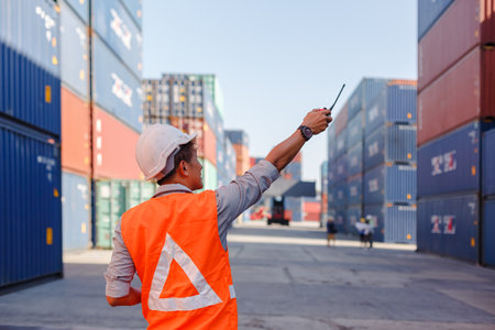 man engineering in uniform wearing safety helmet holding walkie talkie checking containers loading....