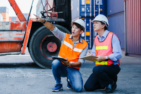 Teamwork engineer foreman, Asian foreman holding clipboard and tablet control loading cargo ship import export, Container terminal cargo. Officers working in container import company.の写真素材